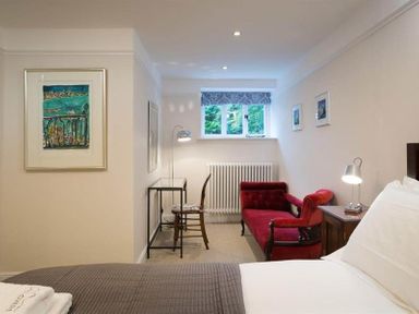 A bedroom with a bed a red sofa a desk with a chair and framed pictures on the walls at Loughrigg Cottage in Ambleside