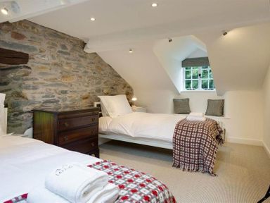 A bedroom with two single beds a stone wall a window seat and a wooden chest of drawers at Loughrigg Cottage in Ambleside
