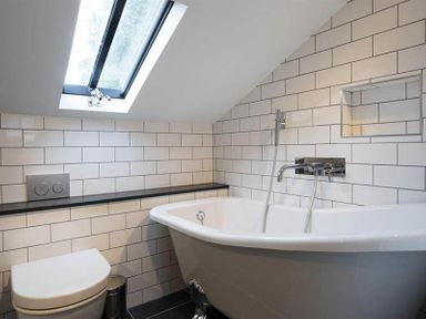 A bathroom with a bathtub a toilet a skylight window and tiled walls at Loughrigg Cottage in Ambleside