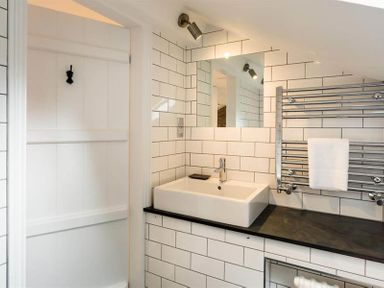 A bathroom with a white sink a mirror towel rail and tiled walls at Loughrigg Cottage in Ambleside