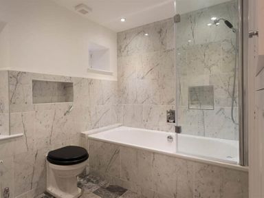 A bathroom with a bathtub shower combination and a toilet with black seat at Loughrigg Cottage in Ambleside
