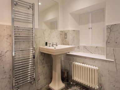 A bathroom with a pedestal sink radiator towel warmer and shuttered window at Loughrigg Cottage in Ambleside