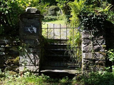 A metal gate between two stone pillars with greenery and a sign saying Loughrigg Cottage in Ambleside