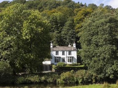 A white house surrounded by trees near a river at Loughrigg Cottage in Ambleside