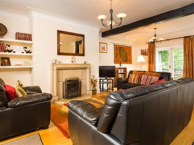 A living room with black leather sofas a fireplace a TV on a stand and orange curtains at Priory Lodge in Windermere
