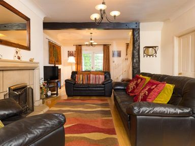 A living room with black leather sofas a fireplace a patterned rug a television a lamp and window with curtains at Priory Lodge in Windermere