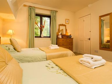 A bedroom with two single beds a wooden dresser a window with curtains and a lamp at Priory Lodge in Windermere