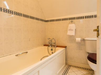 A bathroom with a bathtub a toilet with a wooden seat and patterned tile flooring at Priory Lodge in Windermere