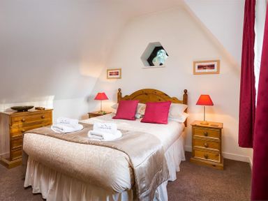 A bedroom with a double bed red pillows wooden bedside tables and lamps Priory Lodge Windermere