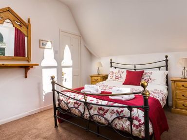 A bedroom with a double bed metal frame wooden nightstands with lamps a mirror on the wall and patterned bedding at Priory Lodge in Windermere