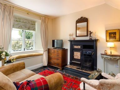 A living room with a window seat a sofa a fireplace a wooden chest of drawers and a red rug at The Blithe Hare in Troutbeck Bridge