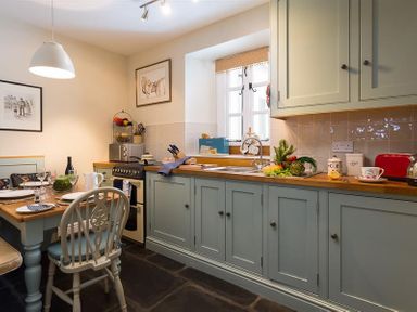 A kitchen with a wooden dining table and chairs light blue cabinets and a window above the sink at The Blithe Hare in Troutbeck Bridge