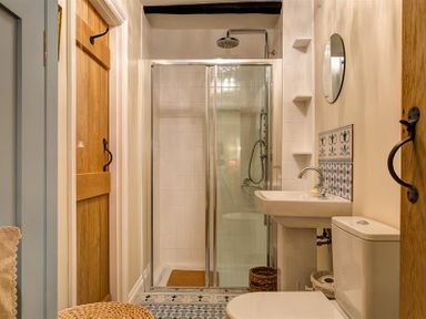 A bathroom with a shower, sink, toilet, wooden doors, and patterned floor tiles at The Blithe Hare in Troutbeck Bridge