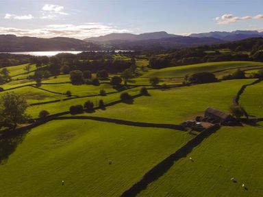 A landscape of green fields with stone fences trees and a barn near a body of water at The Blithe Hare in Troutbeck Bridge