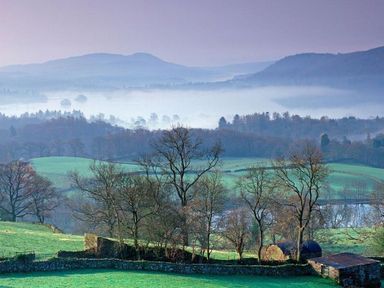 A countryside landscape with green fields trees stone walls and hills in the background at The Blithe Hare in Troutbeck Bridge