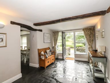 A hallway with a wooden bench and a console table next to an open door with large windows at The Mews in Ambleside