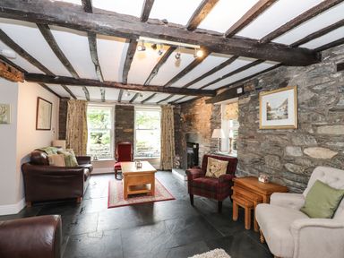 A living room with stone walls wooden beams leather and upholstered chairs and a wooden coffee table at The Mews in Ambleside