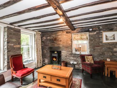 A living room with stone walls a wood burning stove wooden beams on the ceiling and wooden furniture at The Mews in Ambleside