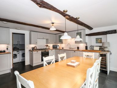 A kitchen with wooden dining table white chairs grey cabinets and exposed wooden beams at The Mews in Ambleside