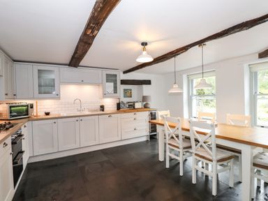 A kitchen with white cabinets wooden countertops a dining table with chairs and exposed ceiling beams at The Mews in Ambleside