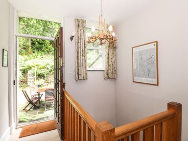 An open wooden door leading to an outdoor patio with chairs and table a staircase with wooden railing and a window with floral curtains inside