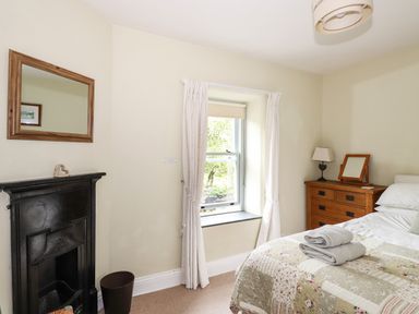 A bedroom with a bed a wooden dresser a window with curtains and a fireplace at The Mews in Ambleside