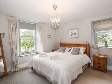 A bedroom with a wooden double bed white bedding two bedside tables and two windows at The Mews in Ambleside