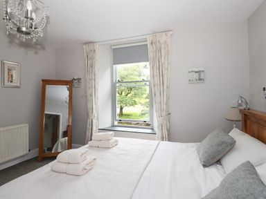 A bedroom with a wooden bed white bedding and folded towels on the bed near a window with curtains and a full-length mirror at The Mews in Ambleside