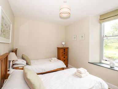 A bedroom with two single beds a wooden drawer and a window at The Mews in Ambleside