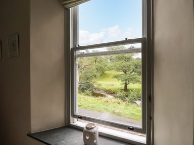 A window open to a view of trees and grass with a white lantern on the windowsill at The Mews in Ambleside