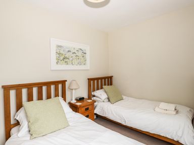 A bedroom with two single wooden beds white bedding a bedside table with a lamp and clock and a framed picture on the wall at The Mews in Ambleside