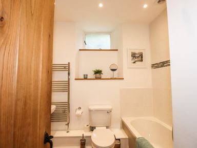 A bathroom with a toilet bathtub towel rack and a small window at The Mews in Ambleside