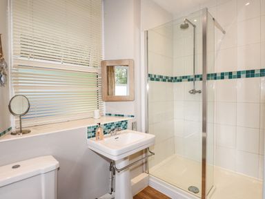 A bathroom with a shower enclosure a white sink a toilet and a window with blinds at The Mews in Ambleside