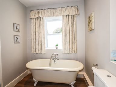 A bathroom with a clawfoot bathtub under a window with curtains and a toilet on the right wall at The Mews in Ambleside