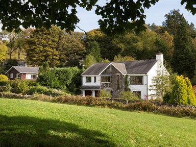 A large house with stone and white walls surrounded by trees and grass at March House in Windermere