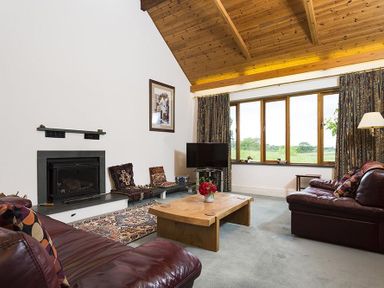 A living room with leather sofas a wooden coffee table a fireplace and a large window at March House in Windermere