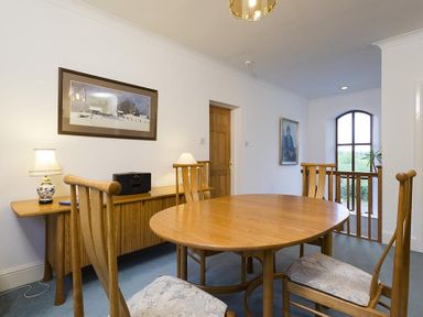 A dining area with a wooden oval table and chairs near a sideboard with lamps and framed pictures at March House in Windermere