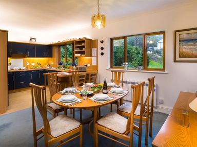 A dining area with a wooden table set for six and a kitchen with blue cabinets at March House in Windermere