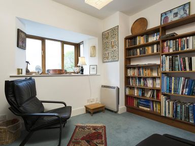 A room with a black chair a bookshelf filled with books and objects on a window sill at March House in Windermere