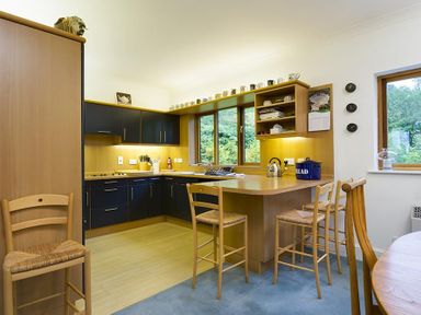 A kitchen with wooden breakfast bar with stools and blue cabinets at March House in Windermere