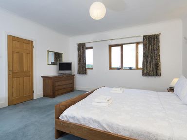 A bedroom with a double bed towels on the bed a wooden dresser with a television and windows with curtains at March House in Windermere