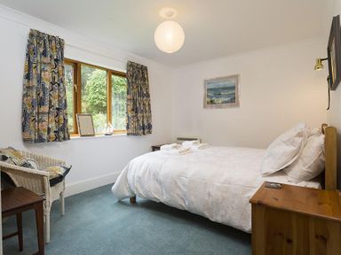 A bedroom with a double bed and folded towels on it beside a window with patterned curtains at March House in Windermere