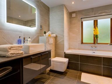 A bathroom with a sink, toilet, bathtub, towels, and a window with flowers at March House in Windermere