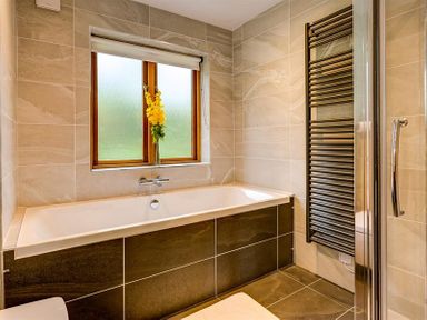 A bathroom with a bathtub below a window and a black towel radiator next to a glass shower door at March House in Windermere