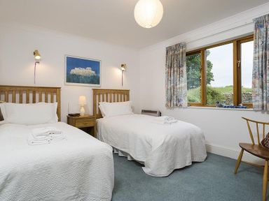 A bedroom with two single beds a wooden chair a window with curtains and a painting on the wall at March House in Windermere