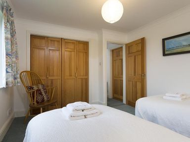 A bedroom with two single beds with white covers wooden wardrobe wooden chair with cushion and a painting on the wall at March House in Windermere