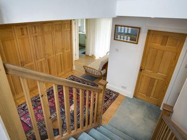 A hallway with wooden stairs blue carpet a wooden door built-in closets a colorful rug and a framed picture at March House in Windermere