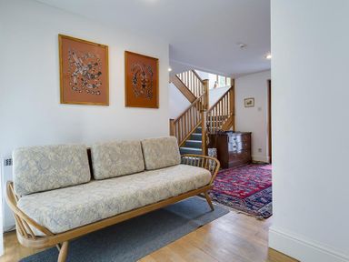 A hallway with a wooden sofa with cushions a staircase a chest of drawers and artwork on the wall at March House in Windermere