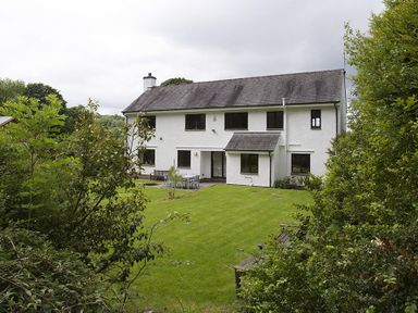 A two-story white house with dark roof and multiple windows surrounded by a green lawn and trees at March House in Windermere