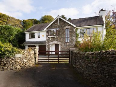 A stone and white house with a gated driveway surrounded by stone walls and greenery at March House in Windermere